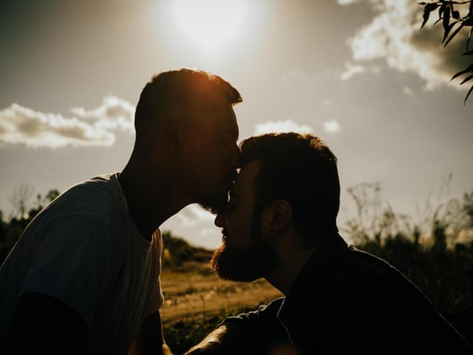 Mann küsst anderen Mann auf die Stirne im Gegenlicht